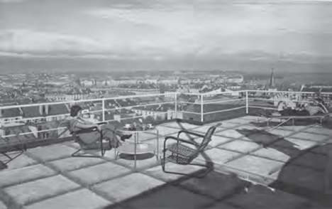 Dachterrasse mit Sitzmöbeln und Person, Panoramablick über Stadt bei bedecktem Himmel, Corbusier